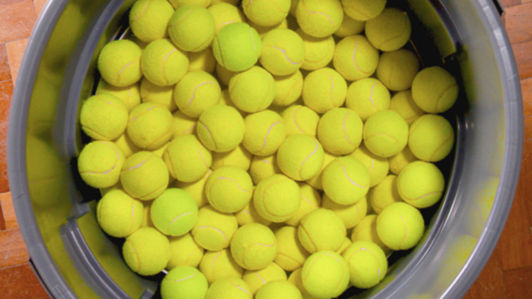 Bucket filled with yellow tennis balls on a wooden floor.