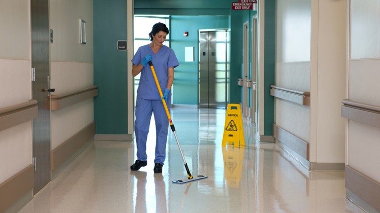 Hospital worker cleaning corridor floor with mop