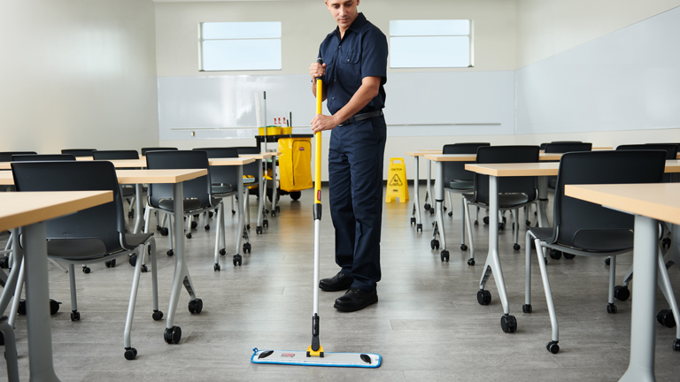 Janitor mopping classroom floor with yellow cleaning cart in the background