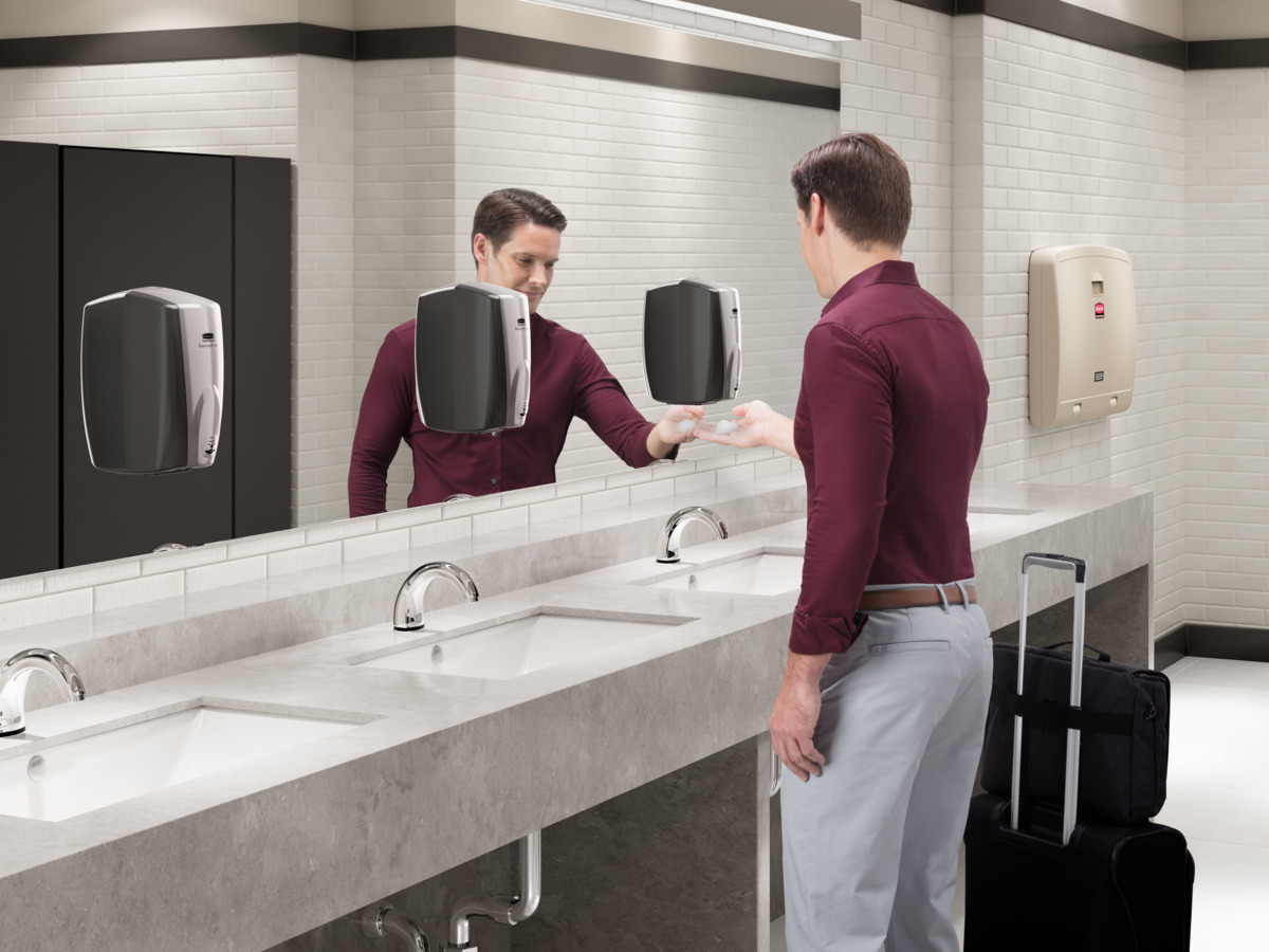 Man in a restroom using a hand soap dispenser