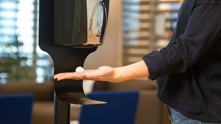 Hand using automatic soap dispenser in a public setting.