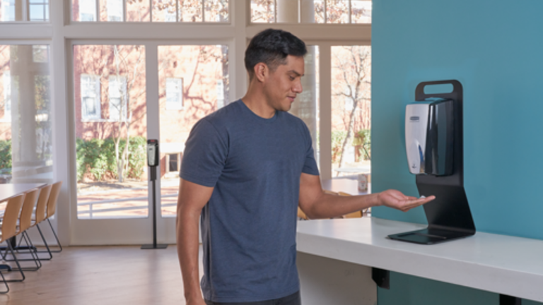 Man using a hand sanitizer dispenser in a bright