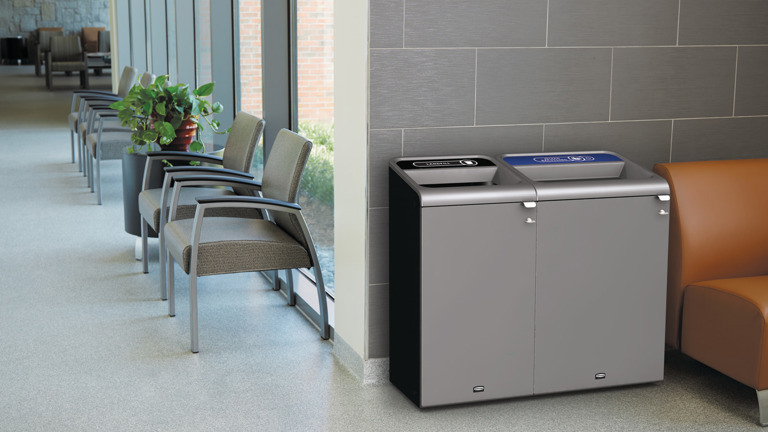 Modern indoor recycling and trash bins in a well-lit waiting area with gray chairs