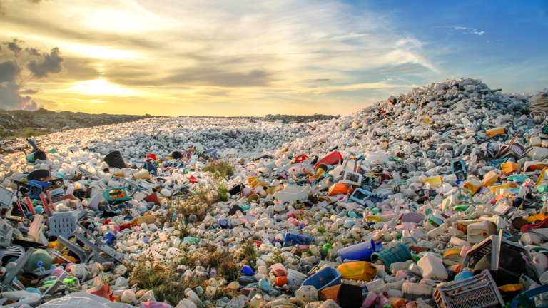 Vast piles of plastic waste in a landfill under a sunset sky.