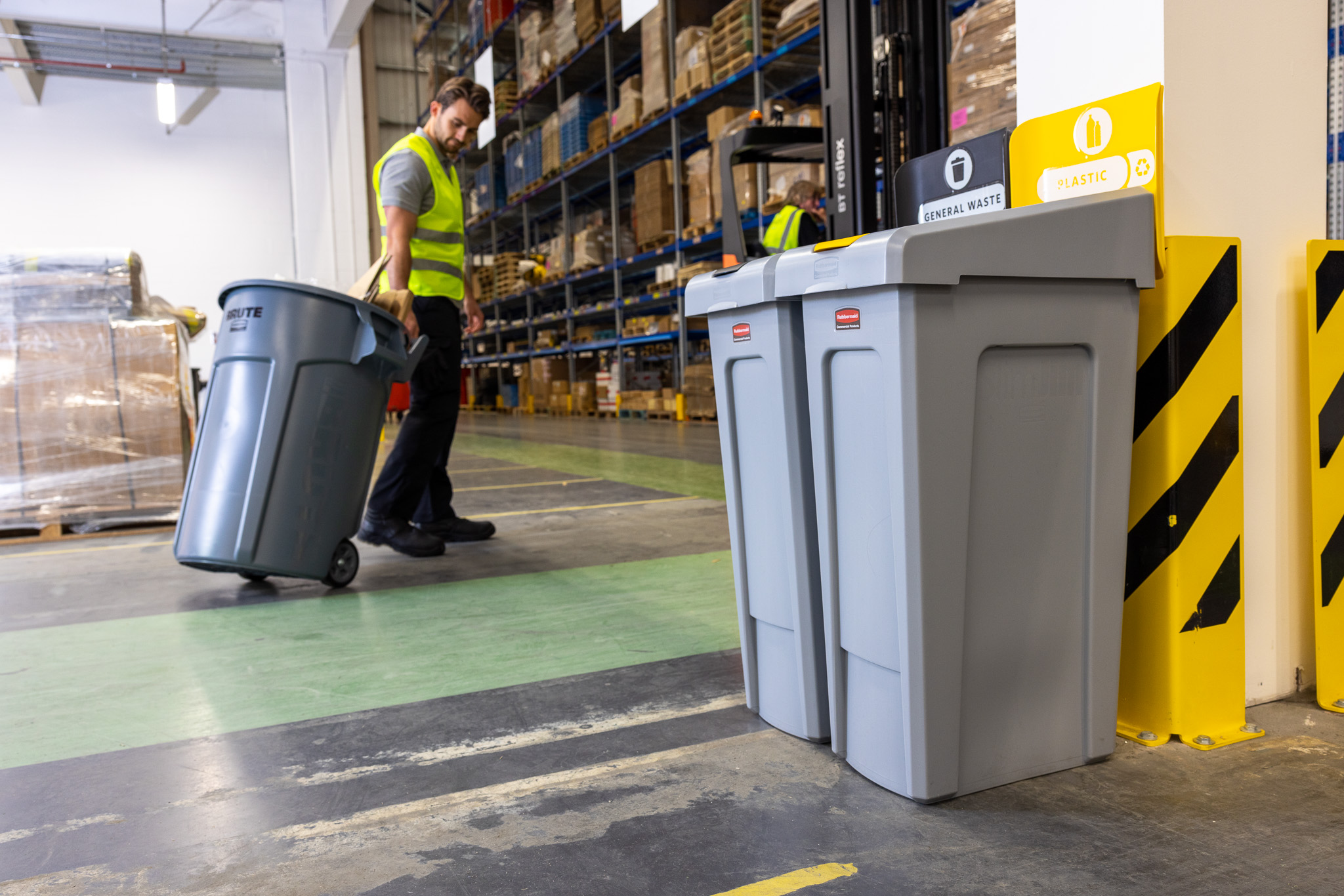 Warehouse worker in high visibility vest moving a large trash bin
